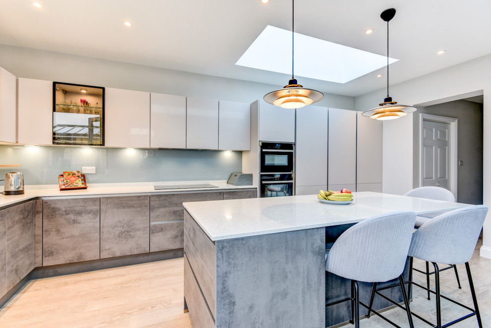 Mid-sized minimalist l-shaped light wood floor and brown floor eat-in kitchen photo in Sussex with an undermount sink, flat-panel cabinets, gray cabinets, granite countertops, blue backsplash, glass sheet backsplash, paneled appliances, an island and white countertops