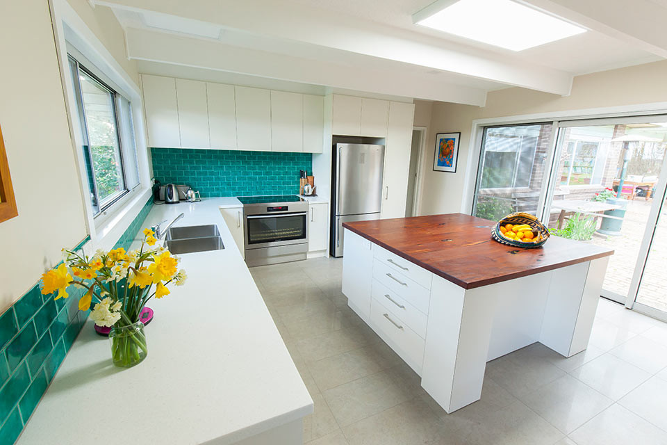 Mid-sized contemporary l-shaped eat-in kitchen in Geelong with a double-bowl sink, flat-panel cabinets, white cabinets, wood benchtops, green splashback, ceramic splashback, stainless steel appliances, ceramic floors and with island.