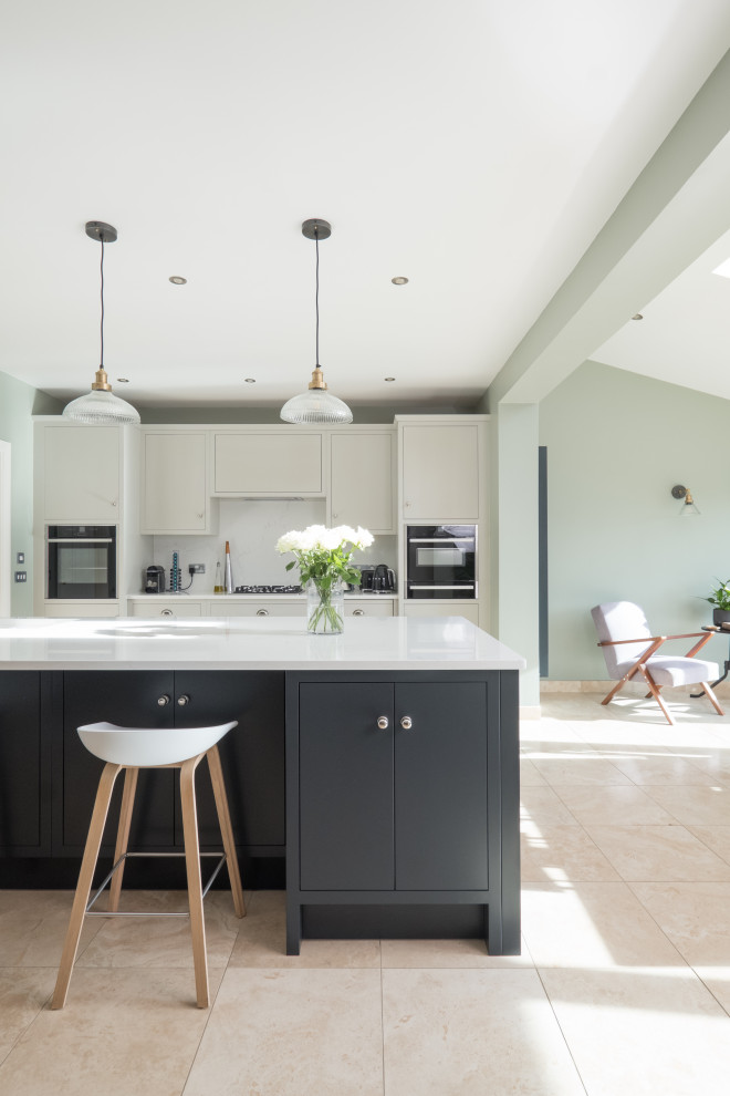 Large traditional single-wall open plan kitchen in Cardiff with an integrated sink, flat-panel cabinets, light wood cabinets, quartzite benchtops, white splashback, engineered quartz splashback, stainless steel appliances, porcelain floors, with island and white benchtop.