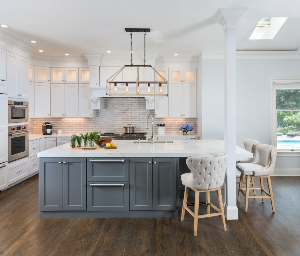 Photo of a large transitional l-shaped kitchen in Boston with an undermount sink, white cabinets, marble benchtops, grey splashback, ceramic splashback, stainless steel appliances, with island, brown floor, shaker cabinets and dark hardwood floors.