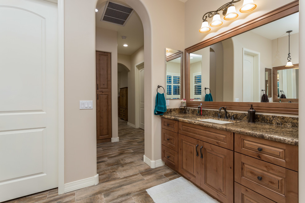Photo of a large country master bathroom in Phoenix with a drop-in sink, recessed-panel cabinets, medium wood cabinets, granite benchtops, a corner tub, an open shower, a one-piece toilet, beige tile, beige walls and terra-cotta floors.