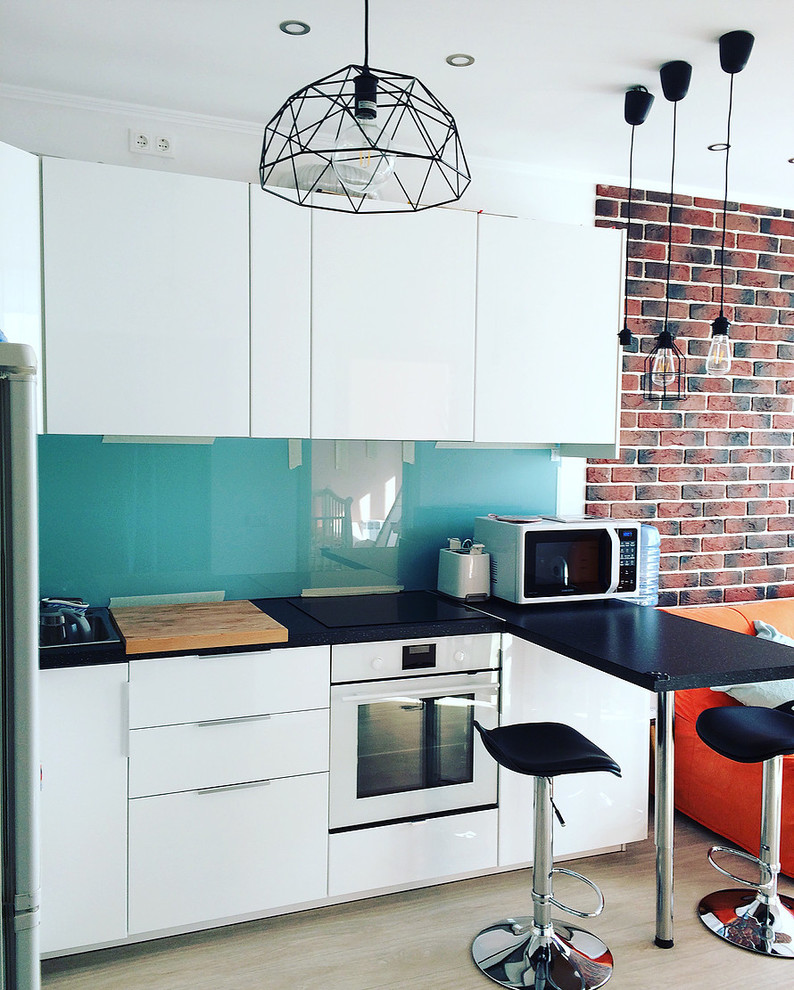 This is an example of a large single-wall eat-in kitchen in Other with a drop-in sink, flat-panel cabinets, white cabinets, solid surface benchtops, blue splashback, glass sheet splashback, white appliances, linoleum floors, with island, beige floor and black benchtop.
