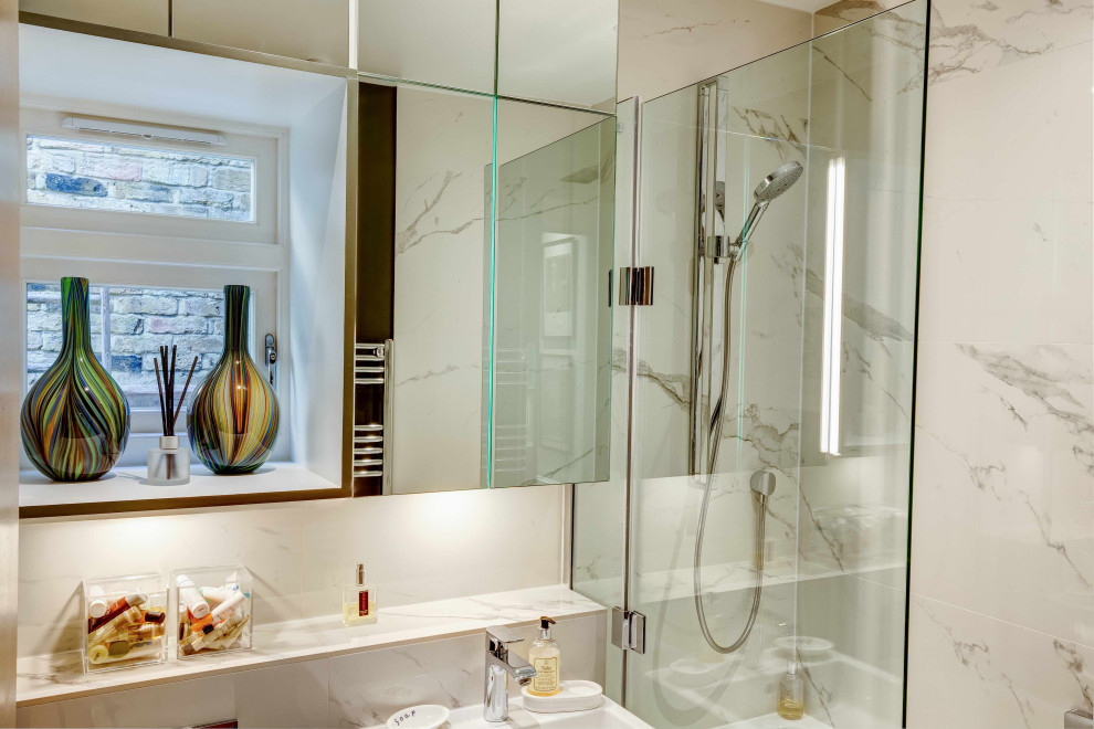This is an example of a small contemporary ensuite bathroom in London with glass-front cabinets, white cabinets, a built-in bath, a shower/bath combination, a wall mounted toilet, white tiles, porcelain tiles, white walls, porcelain flooring, a wall-mounted sink, marble worktops, black floors, a hinged door, white worktops, a wall niche, a single sink, a floating vanity unit and a drop ceiling.