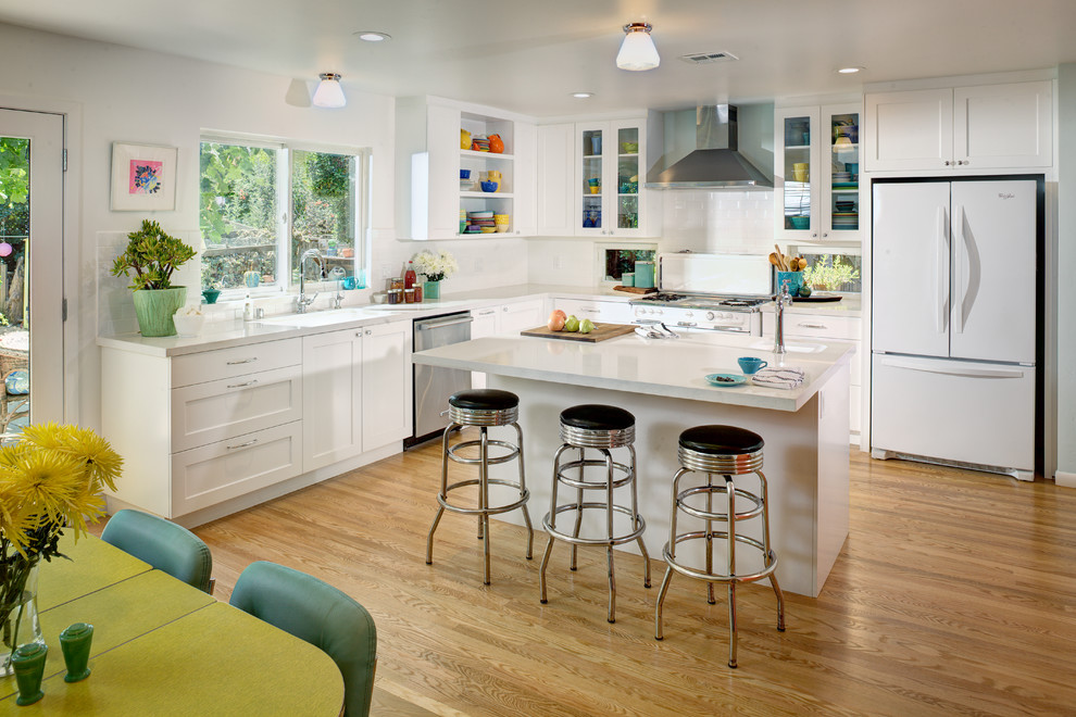 Photo of a transitional l-shaped eat-in kitchen in Sacramento with a drop-in sink, white cabinets, quartz benchtops, white splashback, subway tile splashback, white appliances, with island, shaker cabinets and medium hardwood floors.