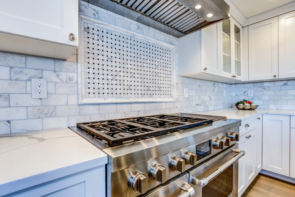 Large modern galley eat-in kitchen in DC Metro with a farmhouse sink, shaker cabinets, white cabinets, quartz benchtops, white splashback, marble splashback, stainless steel appliances, medium hardwood floors, with island, brown floor and white benchtop.