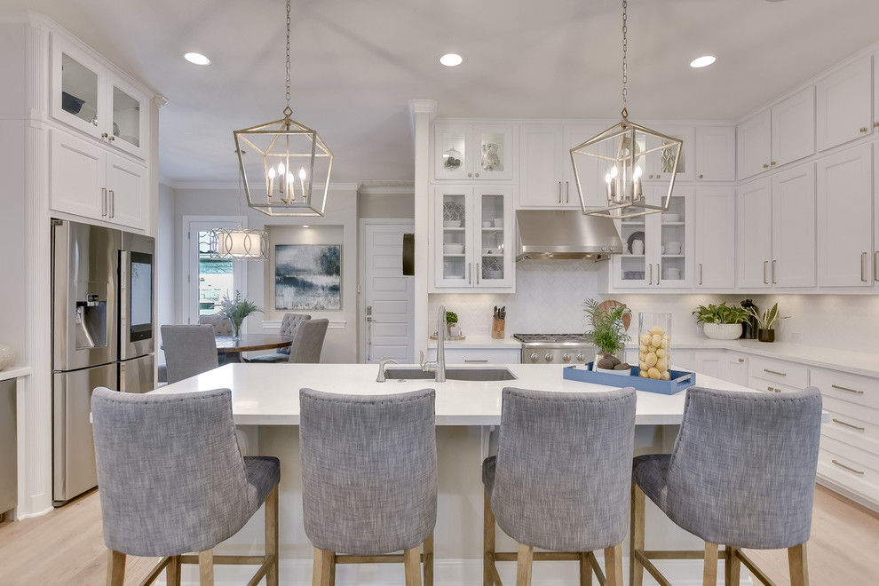 Transitional u-shaped light wood floor and beige floor kitchen photo in Austin with an undermount sink, shaker cabinets, white cabinets, white backsplash, stainless steel appliances, an island and white countertops