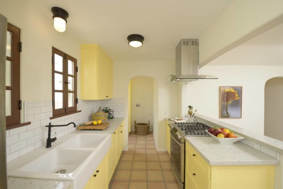 Design ideas for a mid-sized galley eat-in kitchen in Los Angeles with a double-bowl sink, shaker cabinets, yellow cabinets, white splashback, ceramic splashback, stainless steel appliances, terra-cotta floors and no island.