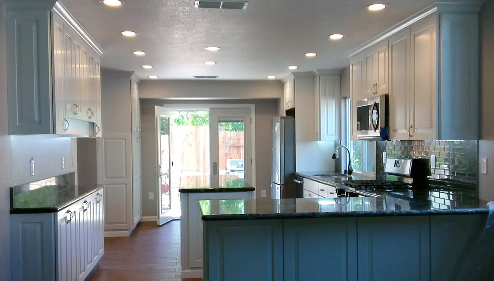 Mid-sized traditional l-shaped eat-in kitchen in Sacramento with an undermount sink, flat-panel cabinets, white cabinets, granite benchtops, black splashback, ceramic splashback, stainless steel appliances, medium hardwood floors and with island.