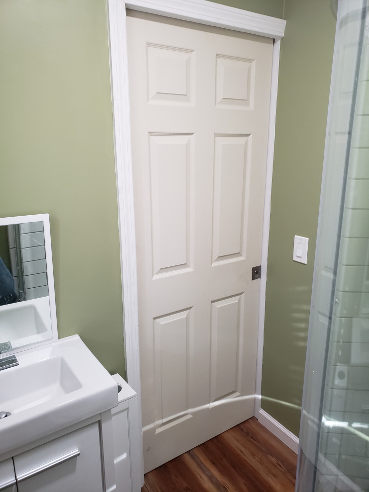 Inredning av ett modernt litet badrum med dusch, med släta luckor, vita skåp, en hörndusch, en toalettstol med separat cisternkåpa, gröna väggar, laminatgolv, ett integrerad handfat, brunt golv och dusch med skjutdörr