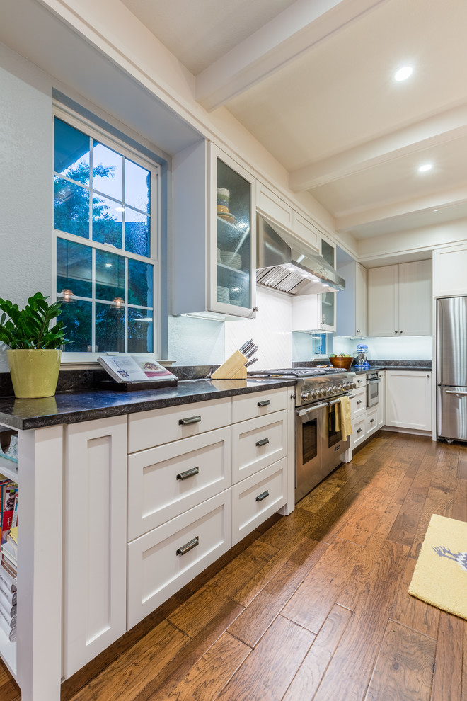 Inspiration for a large transitional l-shaped medium tone wood floor open concept kitchen remodel in Austin with a double-bowl sink, recessed-panel cabinets, gray cabinets, granite countertops, white backsplash, ceramic backsplash, stainless steel appliances and an island