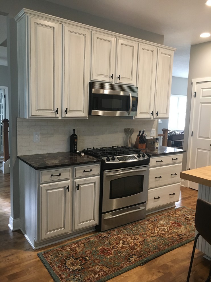 Example of a mid-sized mountain style l-shaped light wood floor and brown floor eat-in kitchen design in Indianapolis with an undermount sink, shaker cabinets, white cabinets, quartzite countertops, gray backsplash, travertine backsplash, stainless steel appliances, an island and black countertops