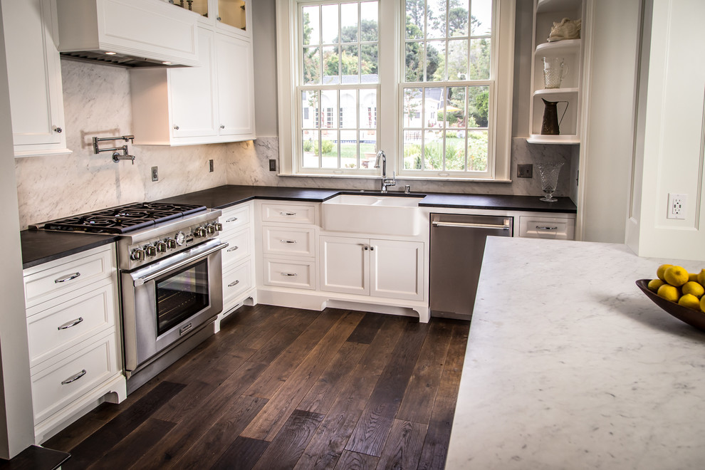 This is an example of a mid-sized arts and crafts l-shaped eat-in kitchen in Santa Barbara with a farmhouse sink, flat-panel cabinets, white cabinets, soapstone benchtops, white splashback, stone slab splashback, stainless steel appliances, dark hardwood floors and with island.
