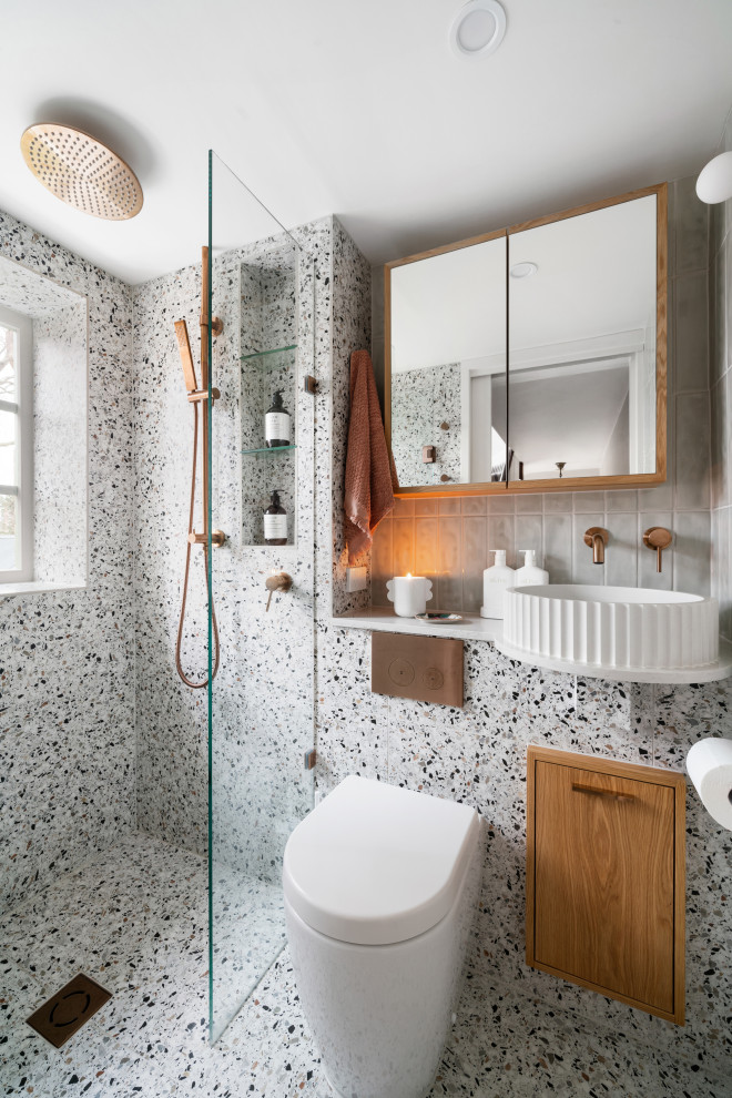 This is an example of a small contemporary master bathroom in Melbourne with shaker cabinets, medium wood cabinets, a drop-in tub, a shower/bathtub combo, a one-piece toilet, multi-coloured tile, porcelain tile, multi-coloured walls, terrazzo floors, a vessel sink, engineered quartz benchtops, multi-coloured floor, a hinged shower door, white benchtops, a single vanity, a built-in vanity, vaulted and planked wall panelling.