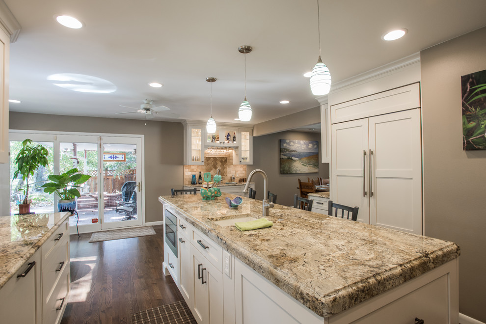 Large transitional u-shaped medium tone wood floor and brown floor eat-in kitchen photo with an undermount sink, shaker cabinets, white cabinets, granite countertops, beige backsplash, travertine backsplash, paneled appliances and an island