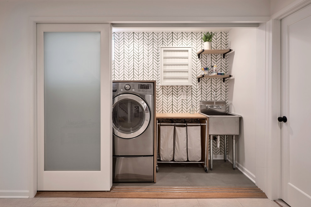 Mid-sized transitional single-wall laundry cupboard in Seattle with an utility sink, wood benchtops, concrete floors, a side-by-side washer and dryer, green floor and grey walls.
