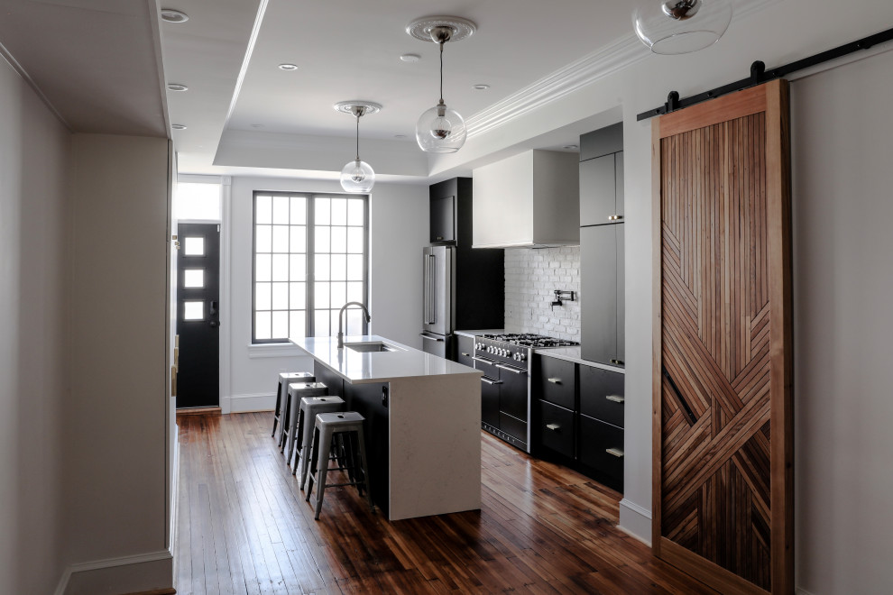 This is an example of a mid-sized contemporary galley eat-in kitchen in Baltimore with an undermount sink, flat-panel cabinets, black cabinets, quartz benchtops, white splashback, brick splashback, stainless steel appliances, medium hardwood floors, with island, brown floor, white benchtop and recessed.