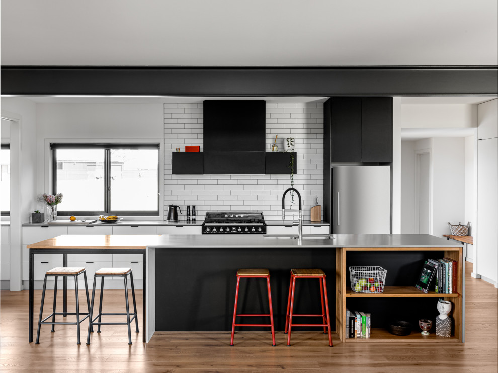 This is an example of a contemporary kitchen in Other with an undermount sink, flat-panel cabinets, white cabinets, white splashback, subway tile splashback, stainless steel appliances, medium hardwood floors, with island and grey benchtop.