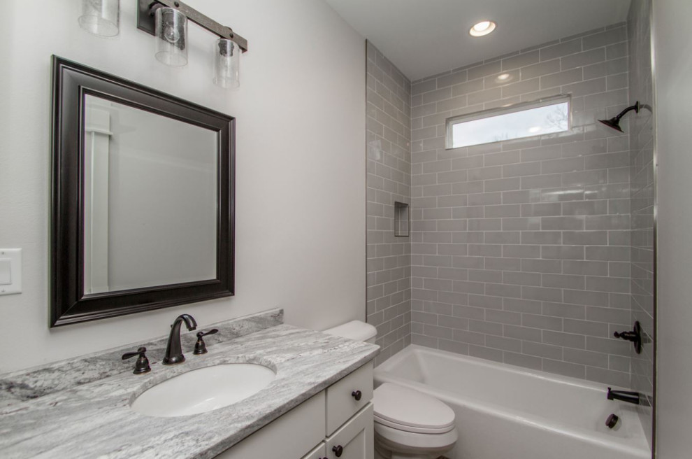 Lantlig inredning av ett litet flerfärgad flerfärgat badrum för barn, med skåp i shakerstil, vita skåp, ett badkar i en alkov, en dusch/badkar-kombination, en toalettstol med separat cisternkåpa, grå kakel, keramikplattor, grå väggar, klinkergolv i porslin, ett undermonterad handfat, granitbänkskiva, grått golv och dusch med duschdraperi