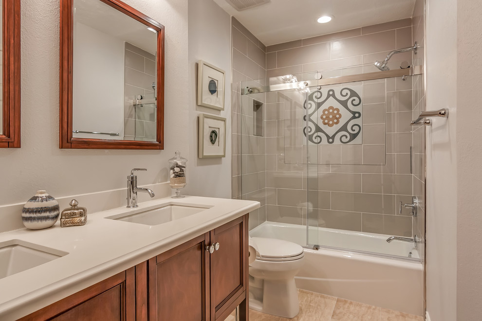 Design ideas for a mid-sized mediterranean 3/4 bathroom in Houston with beaded inset cabinets, medium wood cabinets, an alcove tub, a shower/bathtub combo, gray tile, subway tile, white walls, an undermount sink, beige floor, a sliding shower screen, a two-piece toilet and solid surface benchtops.