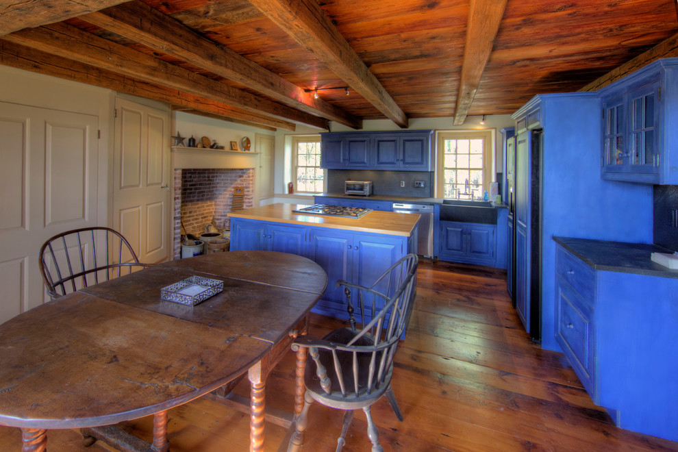 Design ideas for a mid-sized country l-shaped eat-in kitchen in Philadelphia with raised-panel cabinets, blue cabinets, a farmhouse sink, wood benchtops, blue splashback, panelled appliances, dark hardwood floors, with island and slate splashback.