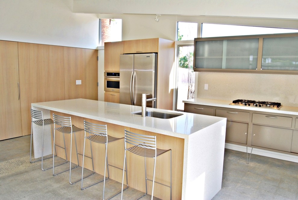 This is an example of a mid-sized midcentury galley eat-in kitchen in Los Angeles with an undermount sink, flat-panel cabinets, light wood cabinets, quartz benchtops, white splashback, stainless steel appliances, concrete floors and with island.