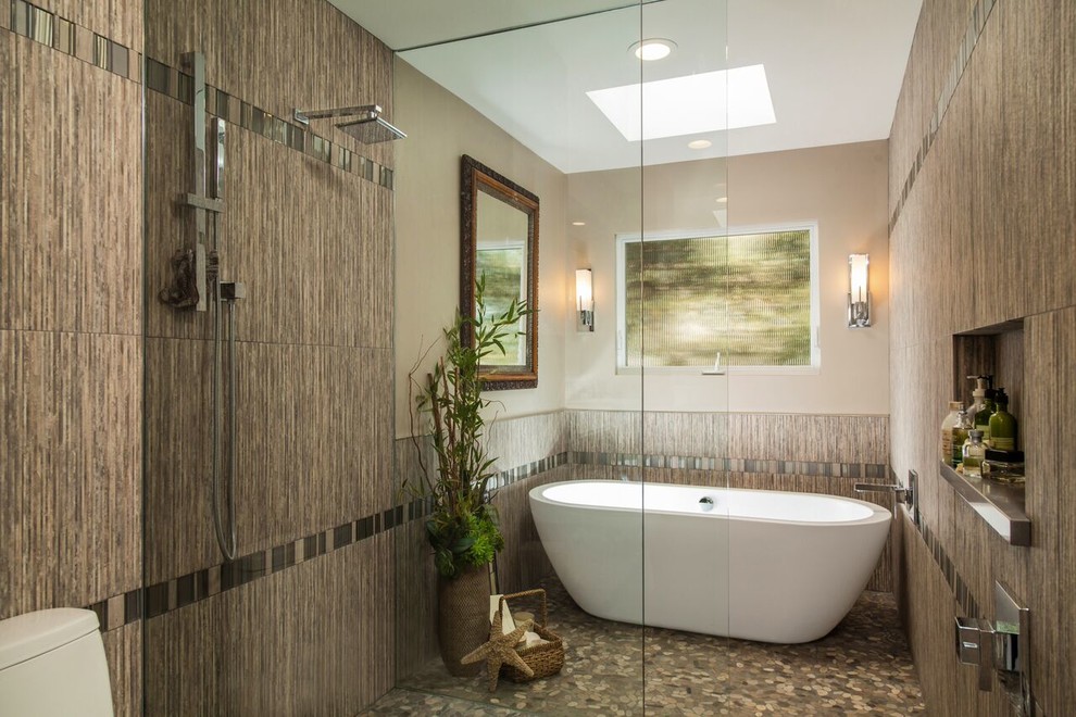 Mid-sized contemporary master bathroom in Los Angeles with a trough sink, flat-panel cabinets, light wood cabinets, engineered quartz benchtops, a freestanding tub, a curbless shower, a one-piece toilet, gray tile, pebble tile, grey walls and pebble tile floors.