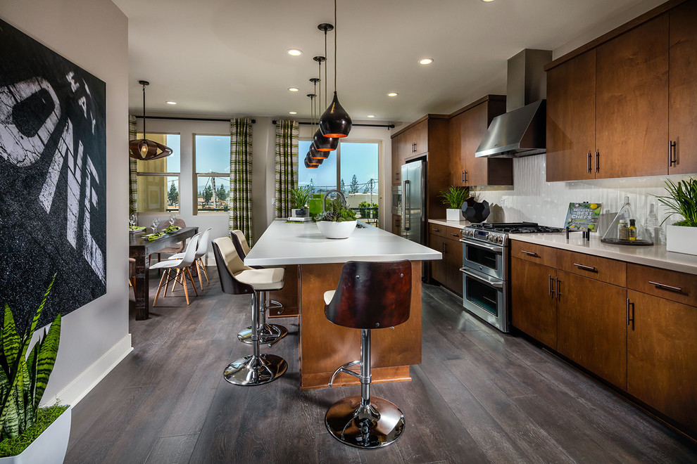 This is an example of a contemporary eat-in kitchen in Los Angeles with flat-panel cabinets, dark wood cabinets, white splashback, dark hardwood floors and with island.