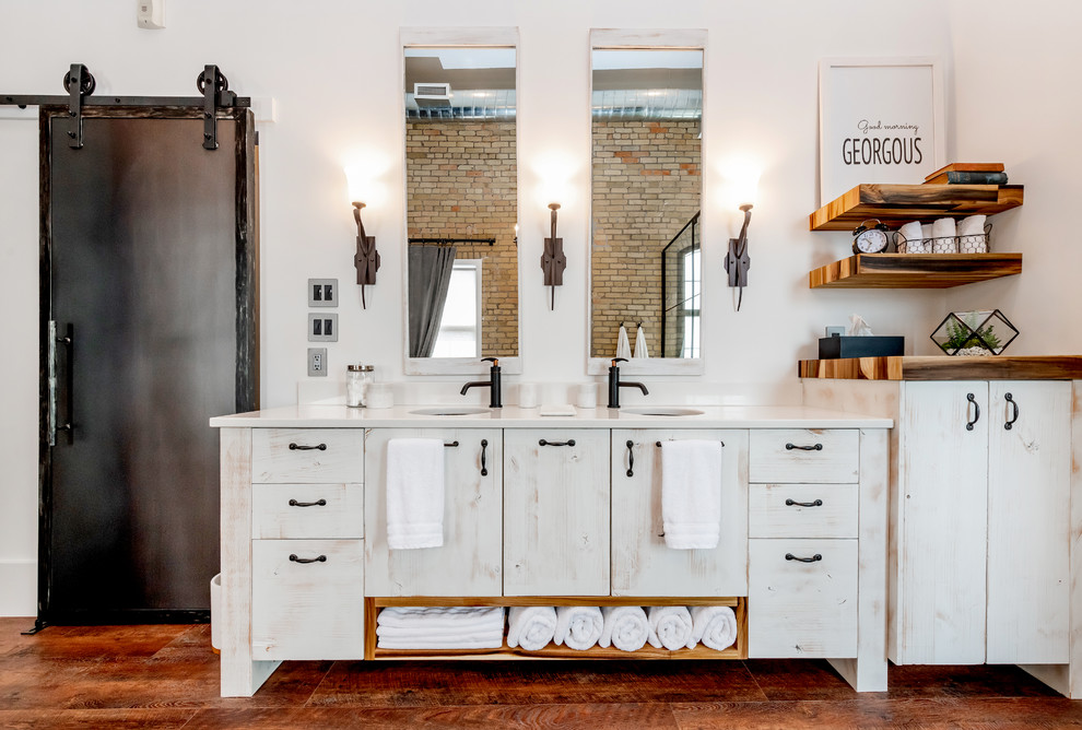 Industrial master bathroom in Other with flat-panel cabinets, distressed cabinets, a freestanding tub, a double shower, a one-piece toilet, gray tile, ceramic tile, white walls, laminate floors, an undermount sink, quartzite benchtops, brown floor, a hinged shower door and white benchtops.