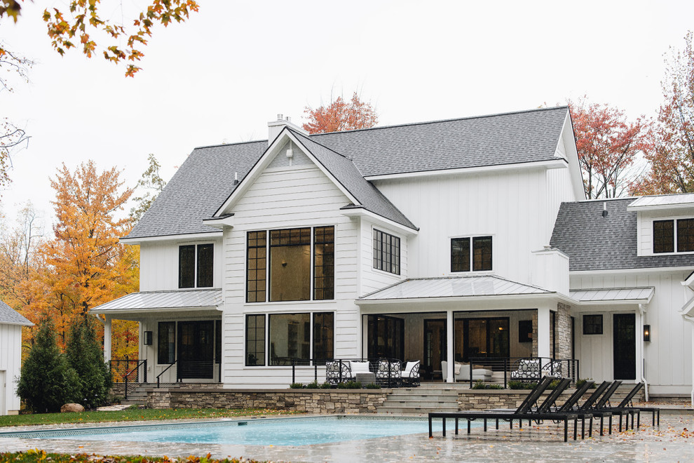 Exterior - Modern farmhouse exterior near Grand Rapids, Michigan featuring a stone patio, in-ground swimming pool, pool deck, board and batten siding, black windows, gray shingle roof, and black doors.
