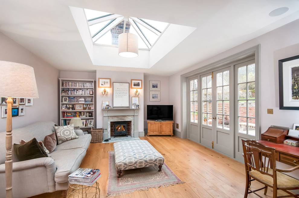 Large transitional enclosed living room in Hampshire with a library, grey walls, medium hardwood floors, a wood stove, a wood fireplace surround, brown floor and a freestanding tv.