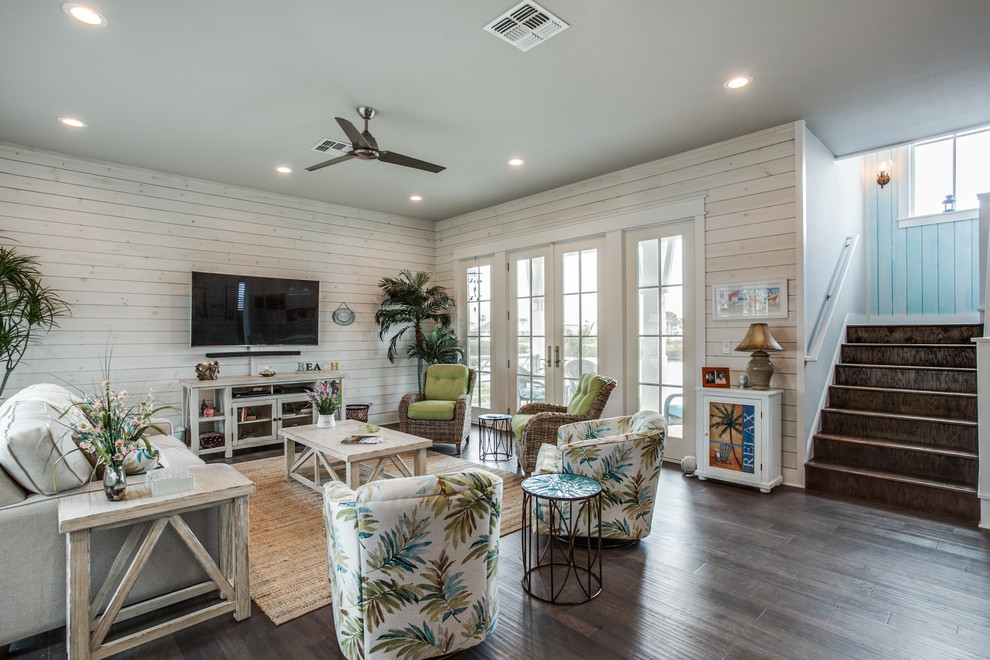 This is an example of a beach style family room in Austin with white walls, dark hardwood floors, no fireplace, a wall-mounted tv and brown floor.