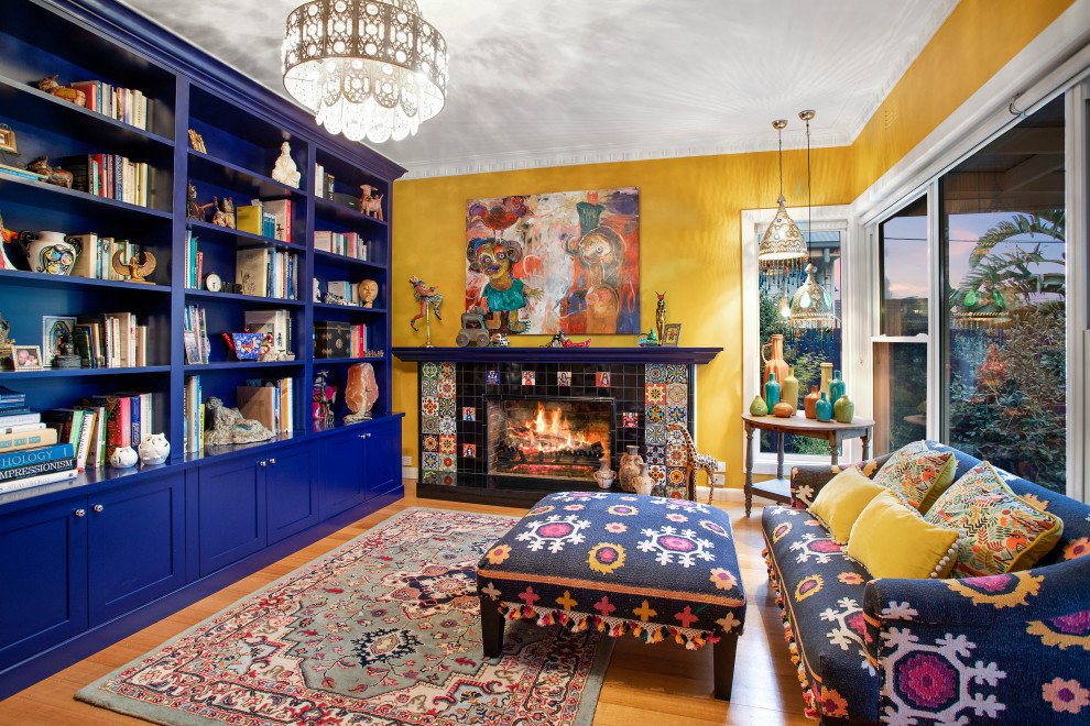 Large eclectic enclosed living room in Melbourne with a library, yellow walls, a standard fireplace, a tile fireplace surround, no tv and light hardwood floors.