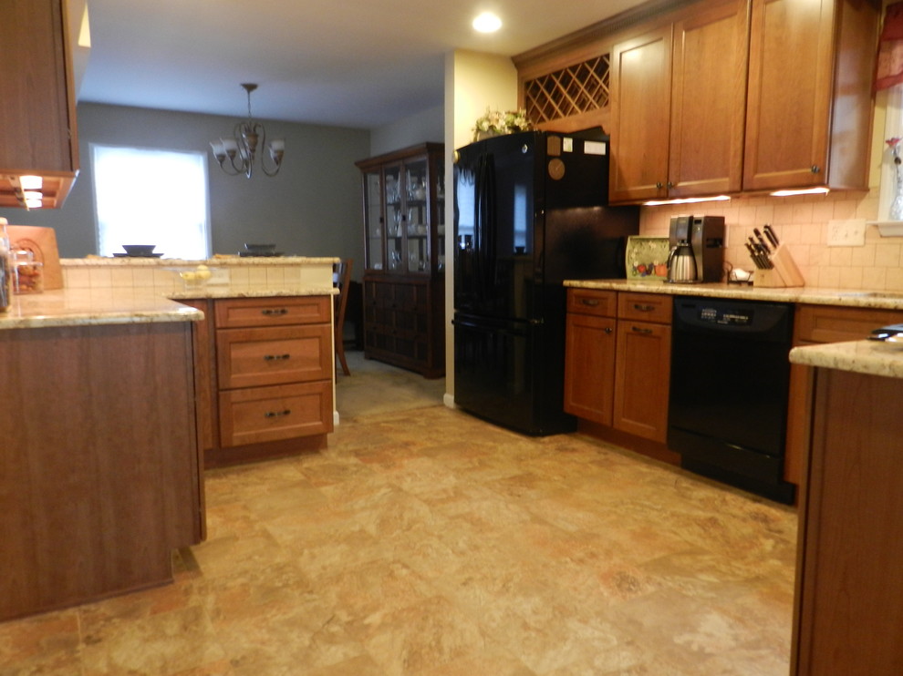 Inspiration for a mid-sized transitional l-shaped porcelain tile eat-in kitchen remodel in New York with a single-bowl sink, recessed-panel cabinets, medium tone wood cabinets, granite countertops, beige backsplash, stone tile backsplash, black appliances, beige walls and a peninsula