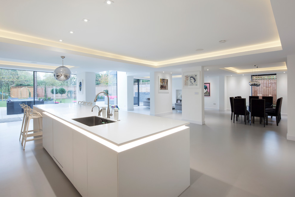 Photo of an expansive contemporary l-shaped open plan kitchen in London with an integrated sink, flat-panel cabinets, white cabinets, concrete benchtops, white splashback, stainless steel appliances and a peninsula.