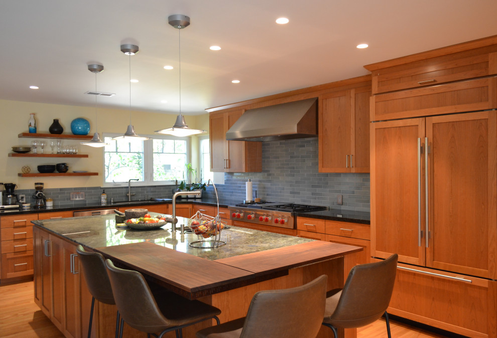 Foto på ett stort amerikanskt turkos kök, med en undermonterad diskho, luckor med infälld panel, skåp i mellenmörkt trä, granitbänkskiva, blått stänkskydd, stänkskydd i tunnelbanekakel, integrerade vitvaror, mellanmörkt trägolv, en köksö och brunt golv