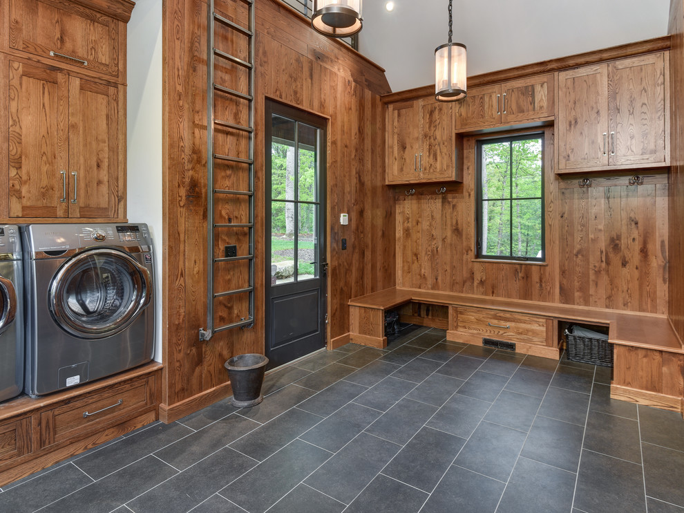 Photo of a large transitional u-shaped utility room in Other with shaker cabinets, medium wood cabinets, a side-by-side washer and dryer, grey floor, brown walls and porcelain floors.