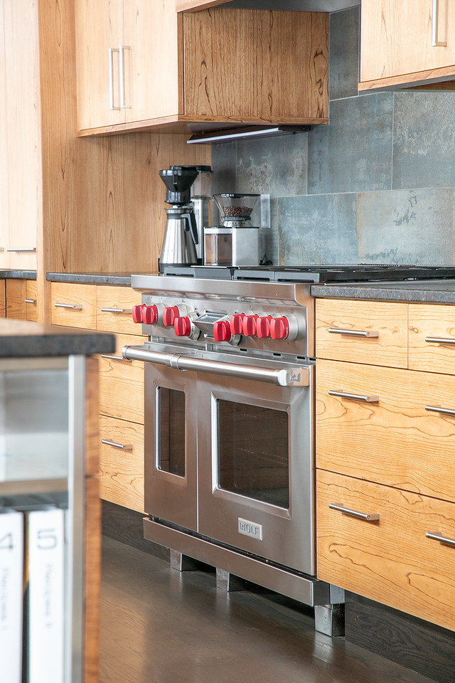 Inspiration for a large rustic l-shaped medium tone wood floor and brown floor open concept kitchen remodel with flat-panel cabinets, light wood cabinets, granite countertops, black backsplash, stainless steel appliances, an island, black countertops, a double-bowl sink and porcelain backsplash