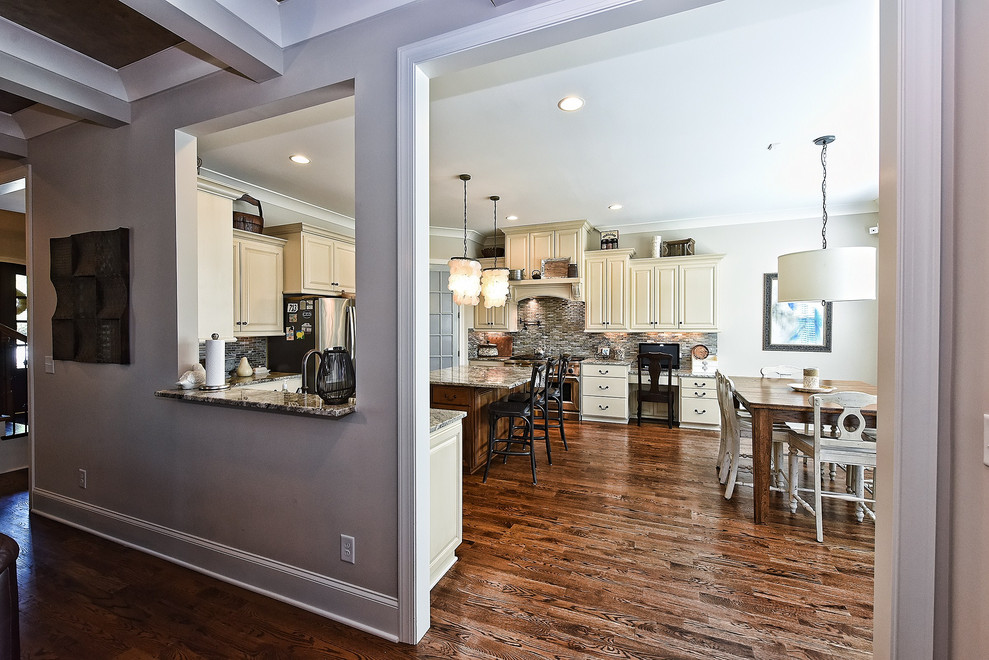 Eat-in kitchen - large transitional u-shaped dark wood floor and brown floor eat-in kitchen idea with a farmhouse sink, raised-panel cabinets, beige cabinets, granite countertops, gray backsplash, matchstick tile backsplash, stainless steel appliances, an island and gray countertops