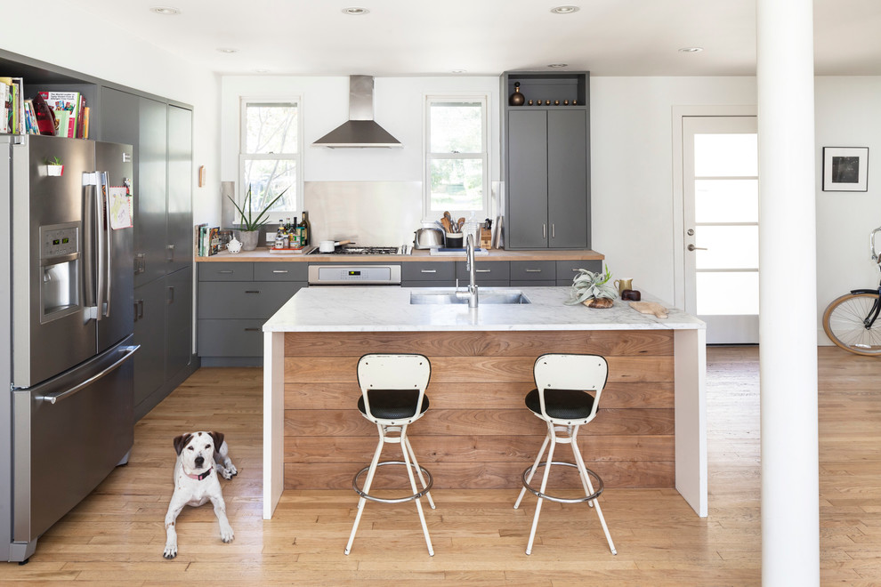 Inspiration for a mid-sized scandinavian l-shaped open plan kitchen in Austin with an undermount sink, flat-panel cabinets, grey cabinets, quartz benchtops, stainless steel appliances, light hardwood floors and with island.