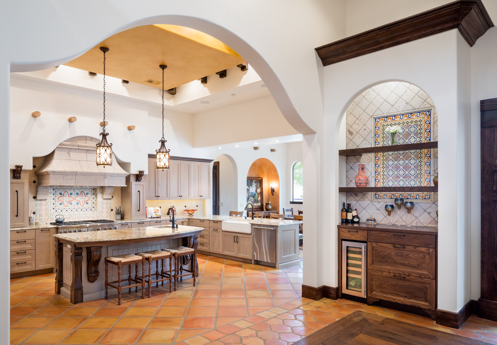 This is an example of a large mediterranean u-shaped eat-in kitchen in Austin with a farmhouse sink, shaker cabinets, light wood cabinets, granite benchtops, multi-coloured splashback, mosaic tile splashback, stainless steel appliances, terra-cotta floors, with island, brown floor and multi-coloured benchtop.