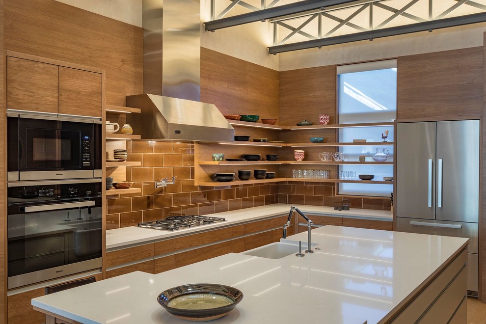Photo of a contemporary l-shaped kitchen in Other with a farmhouse sink, flat-panel cabinets, medium wood cabinets, brown splashback, stainless steel appliances, medium hardwood floors, with island, brown floor and white benchtop.