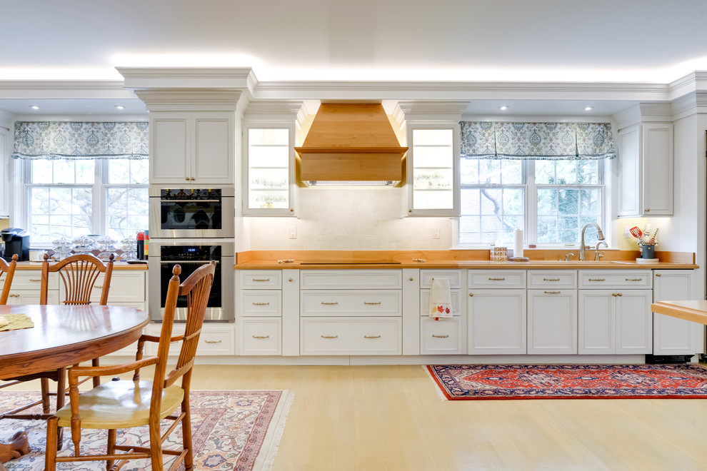 Inspiration for a large traditional single-wall eat-in kitchen in Other with an undermount sink, recessed-panel cabinets, white cabinets, wood benchtops, beige splashback, stainless steel appliances, light hardwood floors, with island, beige floor and brown benchtop.