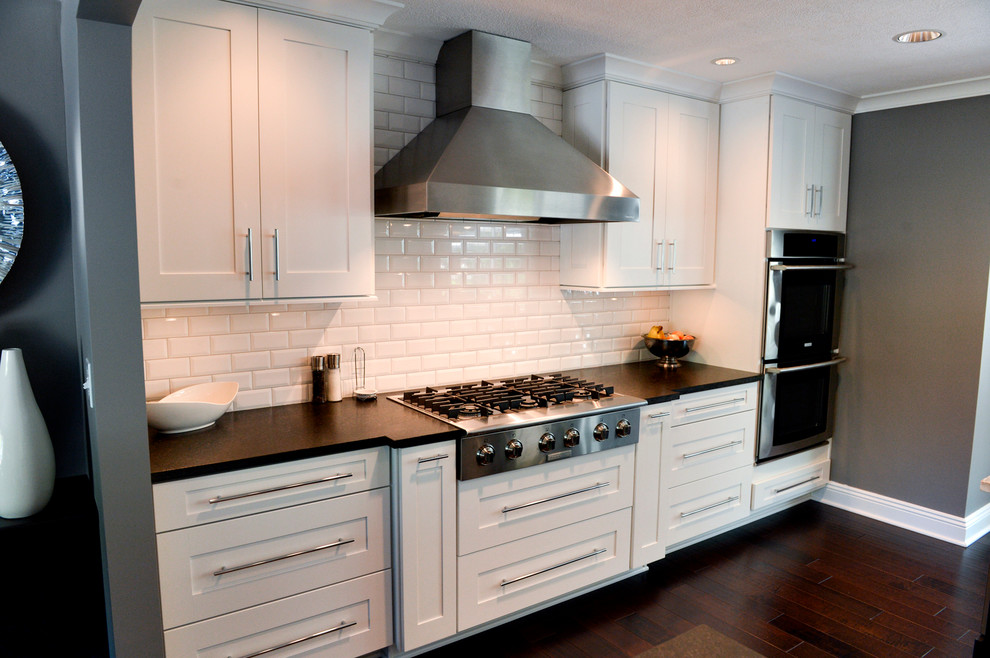 Inspiration for a transitional dark wood floor kitchen remodel in Cleveland with a drop-in sink, recessed-panel cabinets, white backsplash, ceramic backsplash, stainless steel appliances and an island