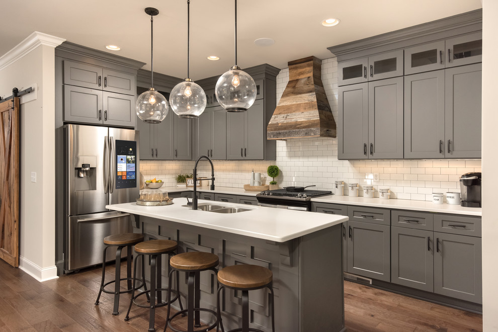 Design ideas for a country l-shaped kitchen in Other with a double-bowl sink, shaker cabinets, grey cabinets, white splashback, subway tile splashback, stainless steel appliances, dark hardwood floors, with island, brown floor and white benchtop.