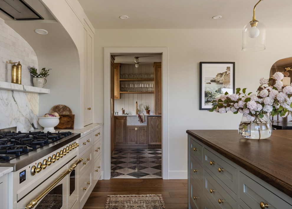 Elegant medium tone wood floor kitchen photo in Seattle with a farmhouse sink, shaker cabinets, beige cabinets, marble countertops, marble backsplash, paneled appliances, an island and white countertops