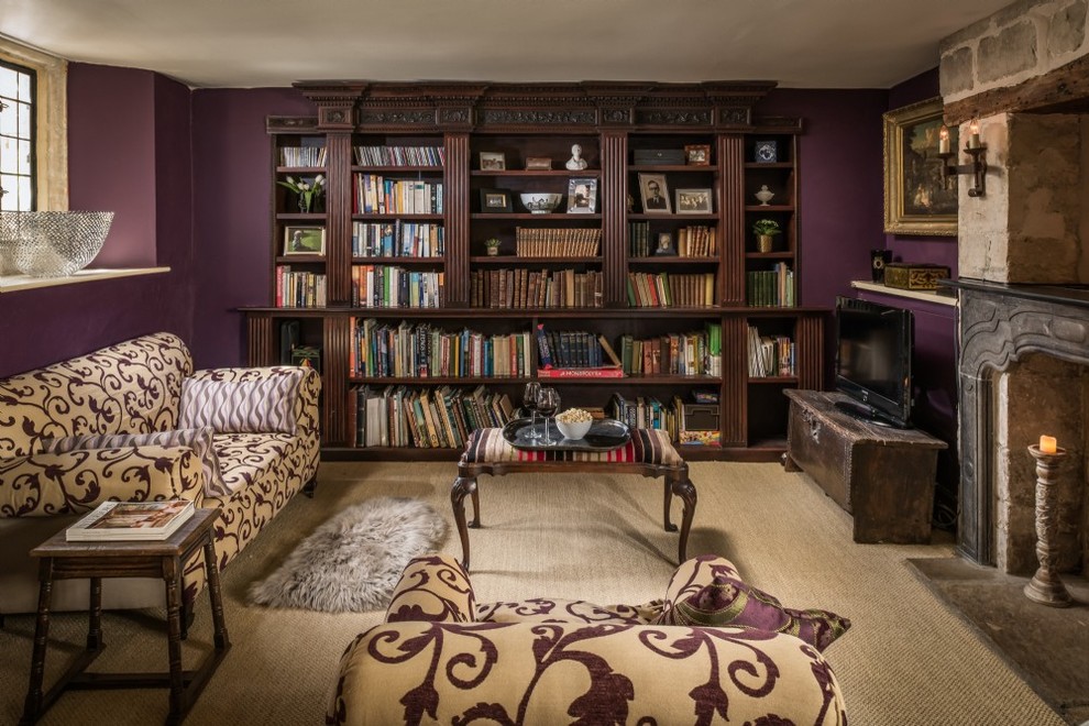 This is an example of a mid-sized traditional enclosed living room in Wiltshire with a library, purple walls, carpet, a standard fireplace, a stone fireplace surround, a freestanding tv and beige floor.