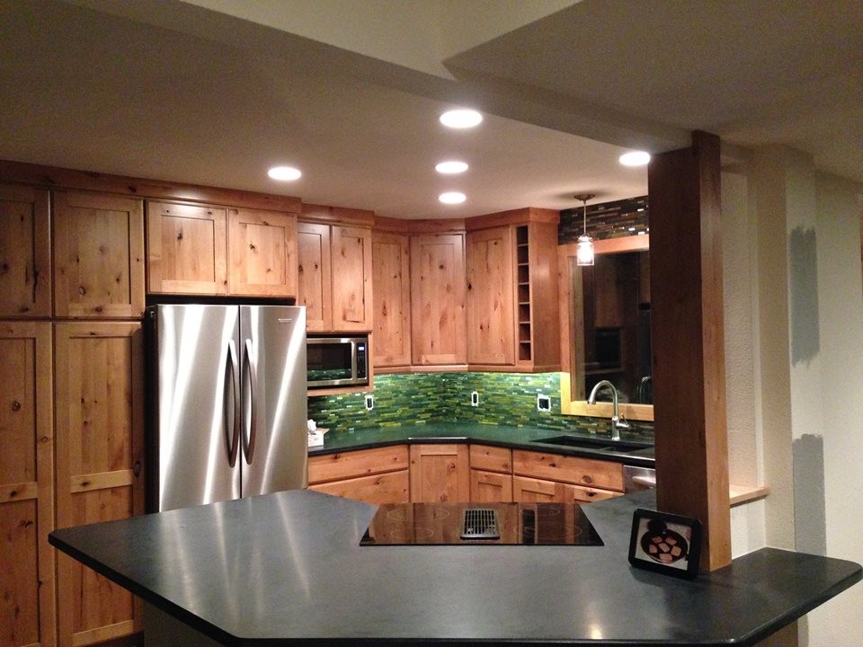 Inspiration for a mid-sized rustic u-shaped dark wood floor eat-in kitchen remodel in Denver with an undermount sink, flat-panel cabinets, light wood cabinets, granite countertops, green backsplash, glass tile backsplash, stainless steel appliances and a peninsula