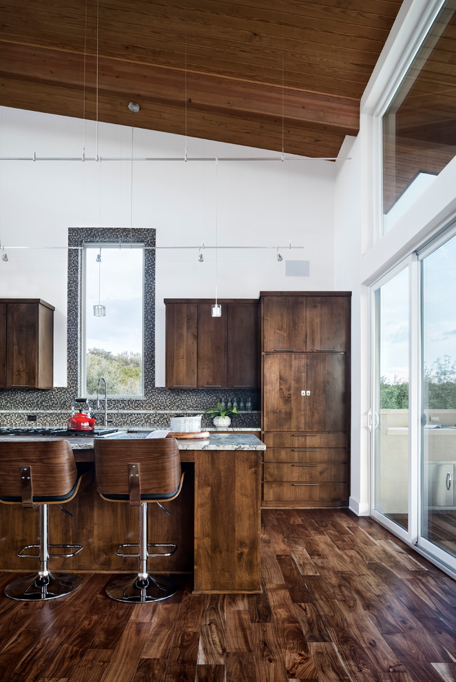 Photo of a mid-sized contemporary galley open plan kitchen in Austin with an undermount sink, flat-panel cabinets, dark wood cabinets, grey splashback, mosaic tile splashback, with island and dark hardwood floors.
