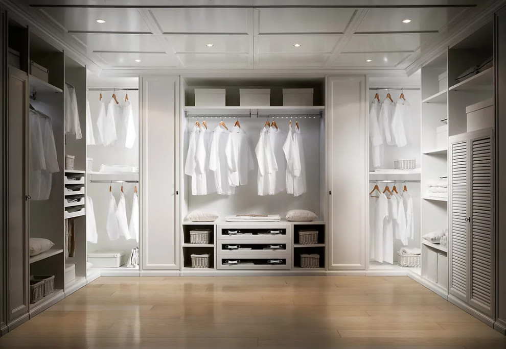 Inspiration for a mid-sized gender-neutral walk-in wardrobe in New York with louvered cabinets, white cabinets, light hardwood floors, brown floor and wood.
