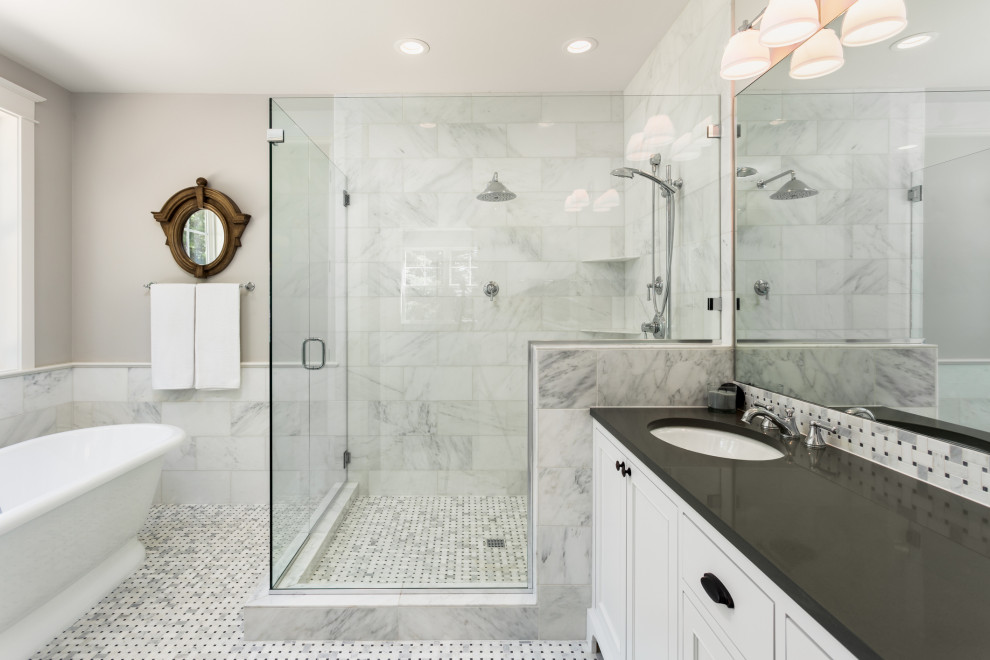 This is an example of a mid-sized transitional master bathroom in New York with shaker cabinets, a freestanding tub, a double shower, black and white tile, stone tile, marble floors, an undermount sink, soapstone benchtops, white floor, a hinged shower door and black benchtops.